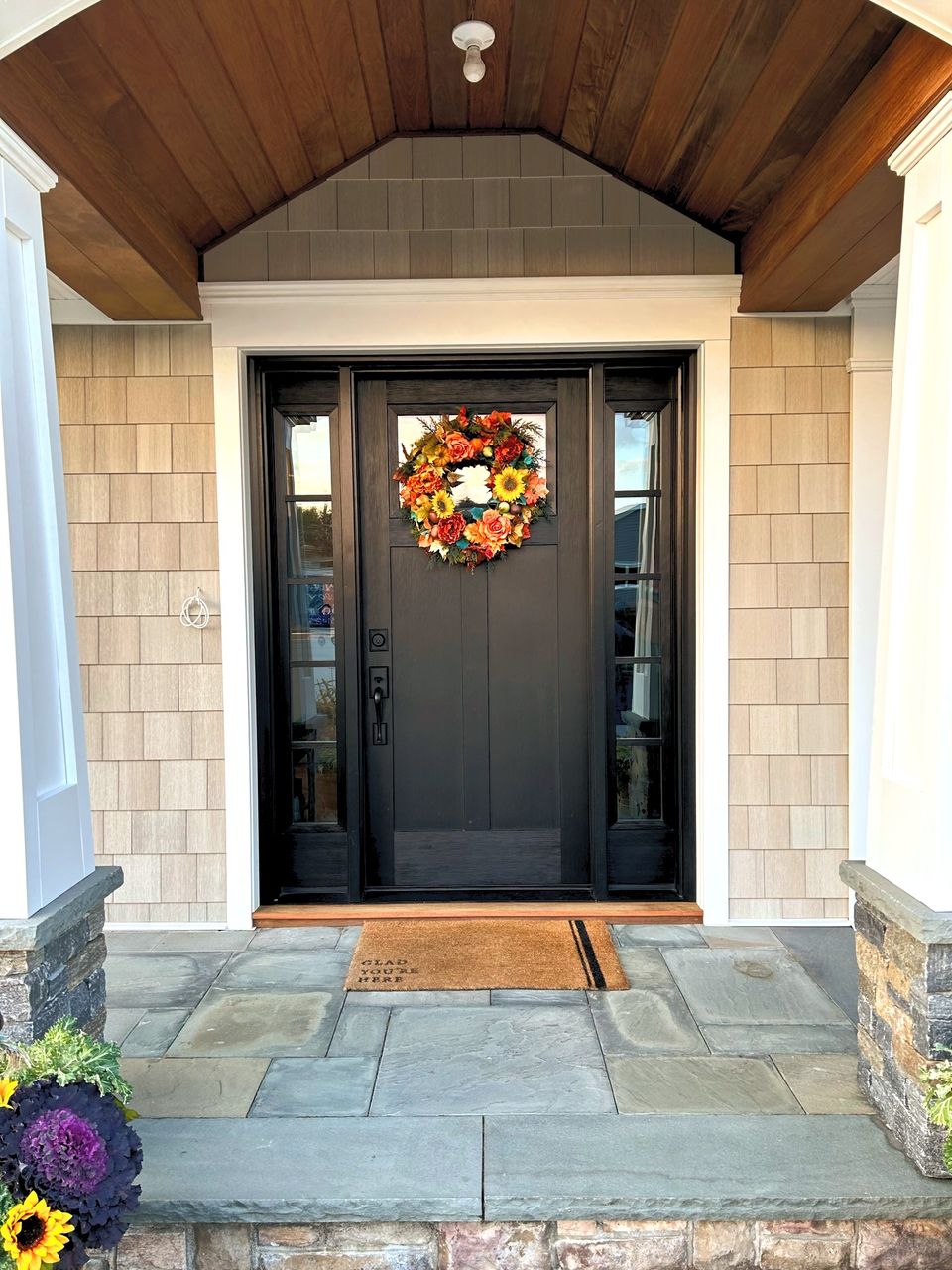 Black front door with sidelights, shingle walls, and a bluestone landing