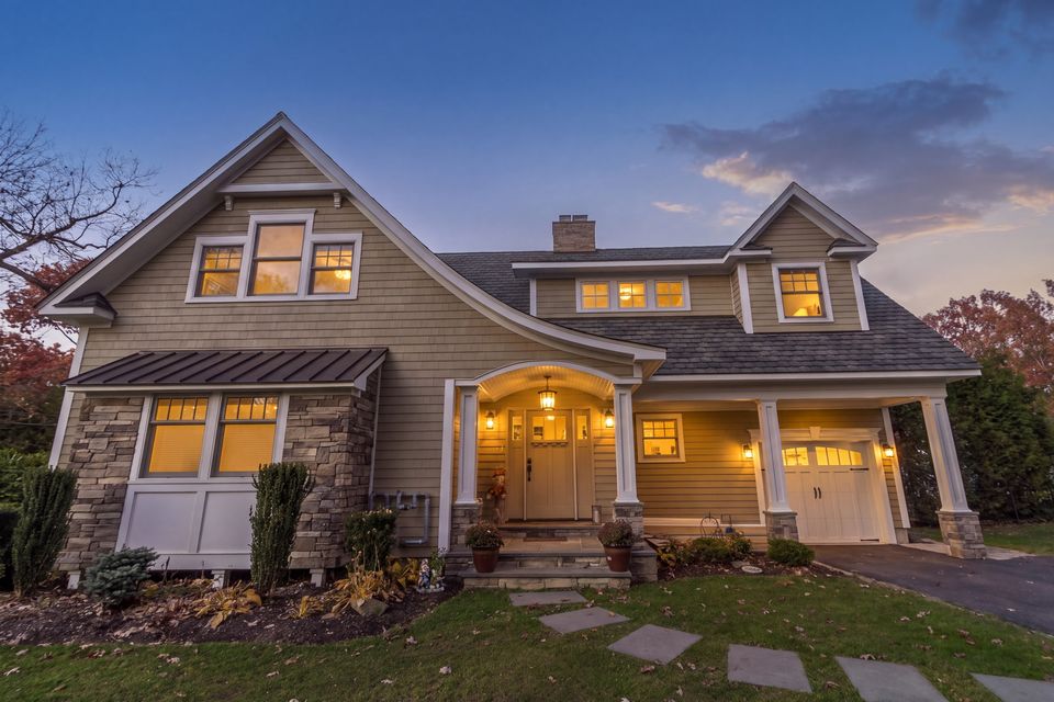 Craftsman style home with shingle siding, stone, and lit windows at twilight