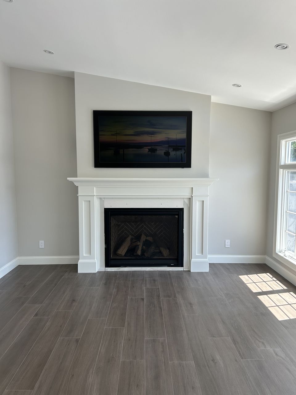 Living room with a white fireplace mantel, a vaulted ceiling, and wide plank floors
