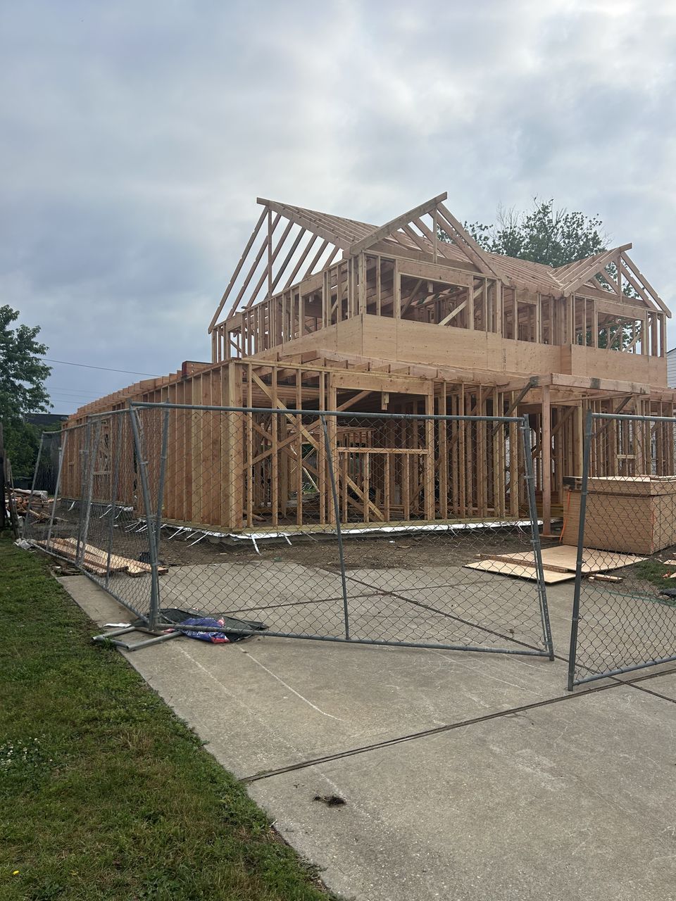 New build framing behind a temporary fence at the end of a driveway