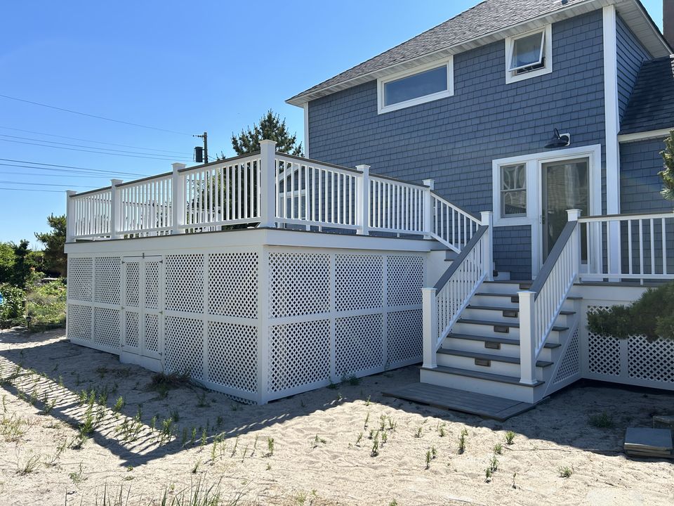 Raised deck with white vinyl rails, lattice skirting, and stairs up to the back door