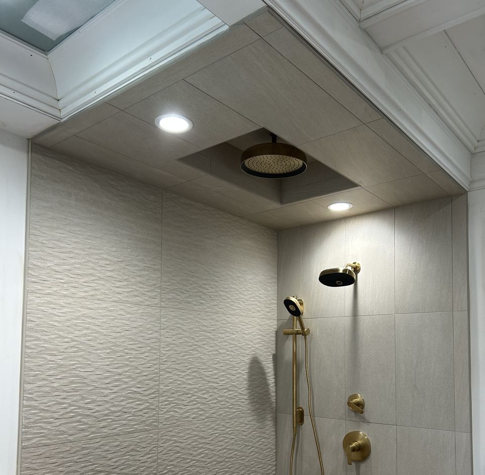 Tiled shower with brass fixtures under a recessed rain head