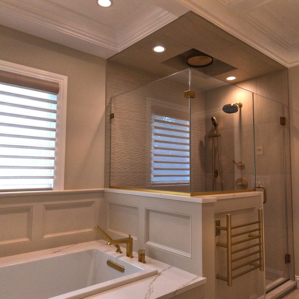 The finished primary bath: a glass shower with brass fixtures, a new tub, and paneled walls under a coffered ceiling