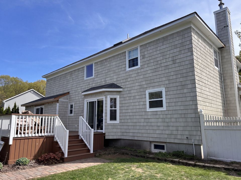 Rear of the rebuilt house in cedar shake with white trim, a bay window, and the deck