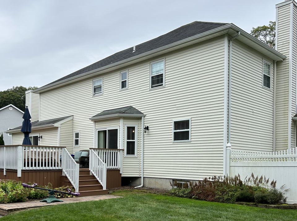 Before: rear of the house in white vinyl siding, with the deck and stairs