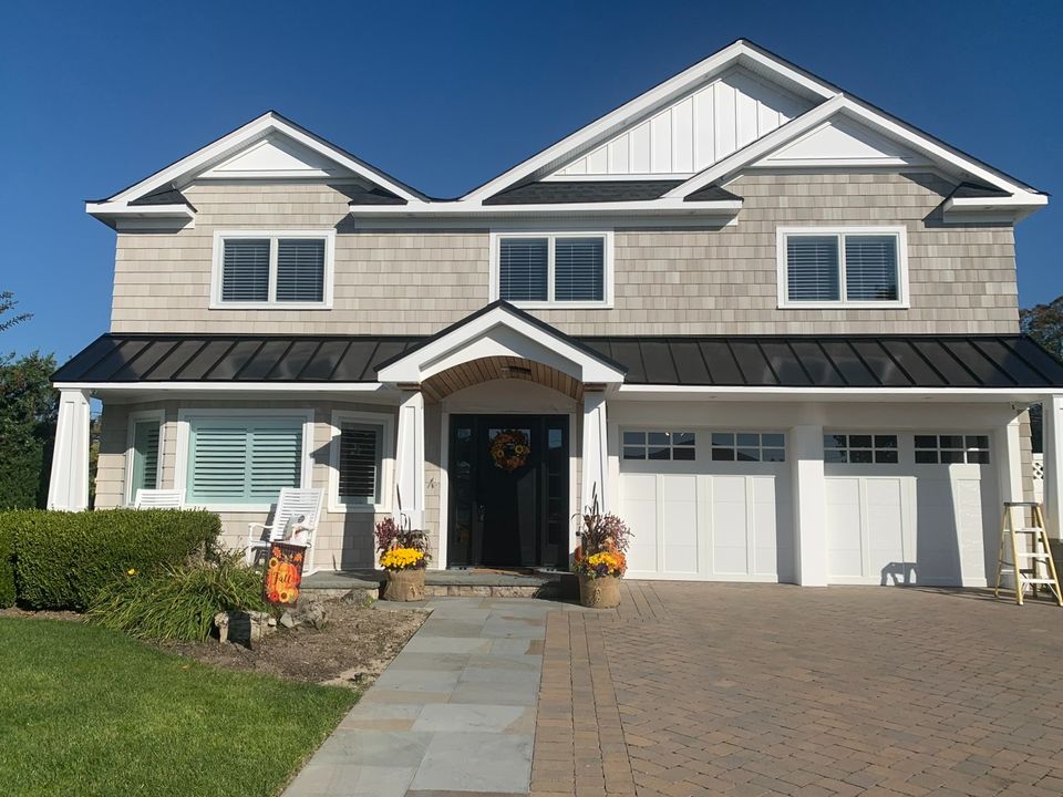Two story shingle colonial with a covered front porch and a paver driveway